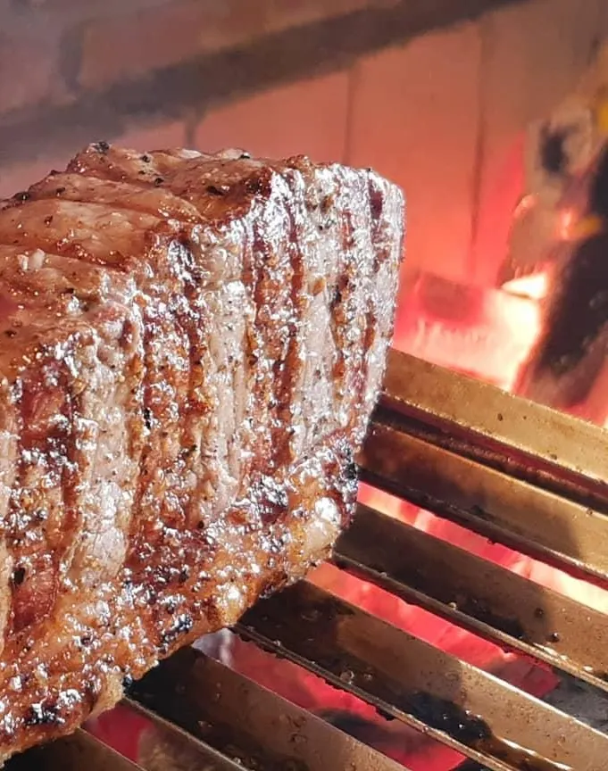 Peça de carne selando na grelha sobre brasa