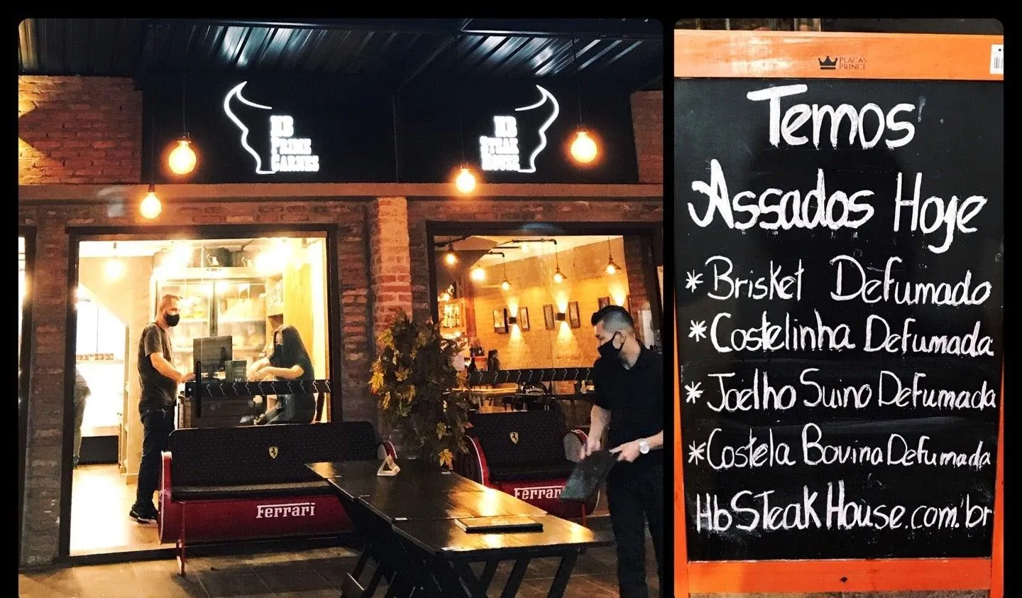 Entrada da HB à noite com a lousa anunciando brisket, costelinha, joelho suíno e costela bovina defumados